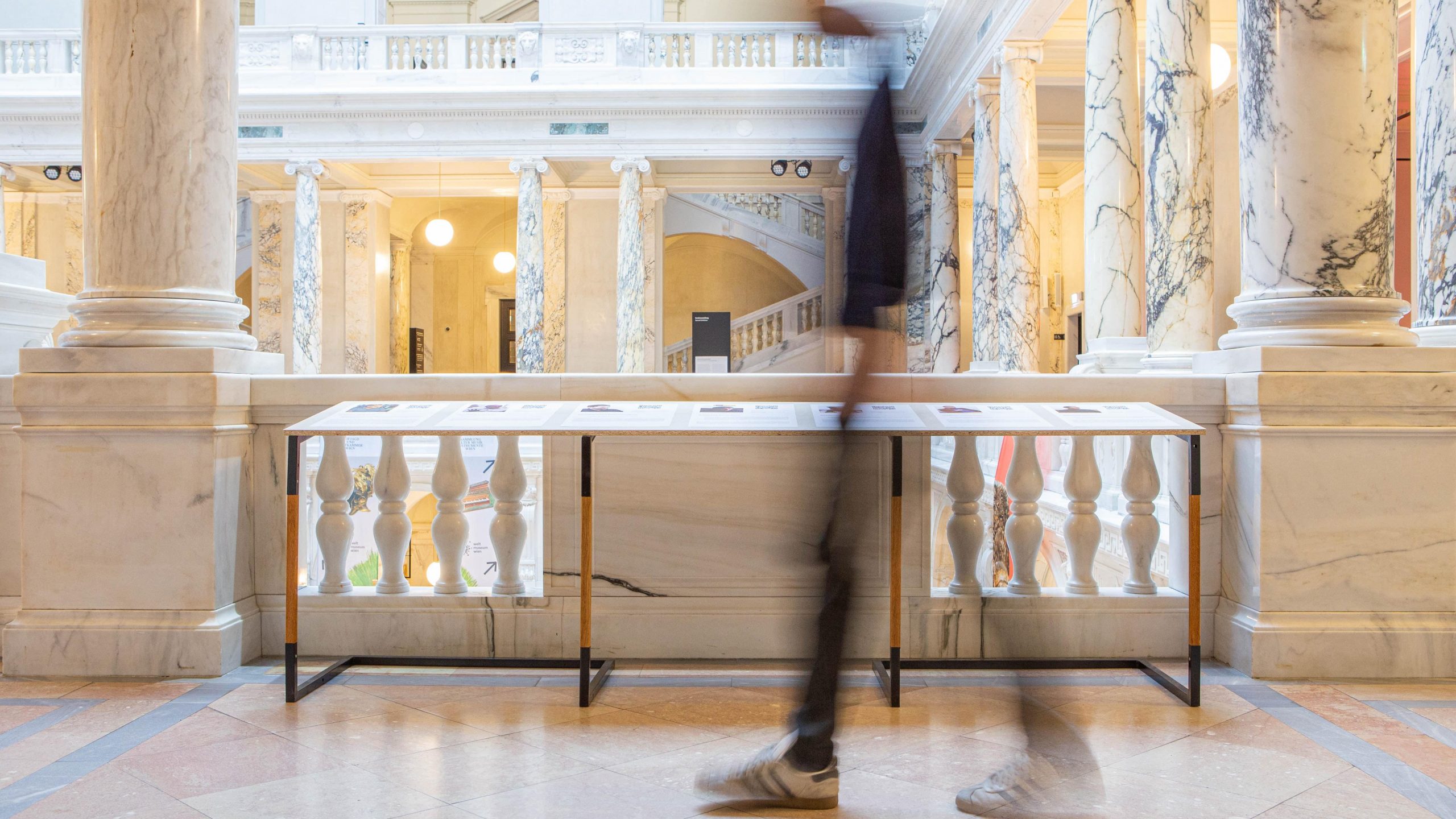 Auf dem Bild ist das Weltmuseum Wien zu sehen. Ein Mensch läuft an einem Ausstellungstisch vorbei.